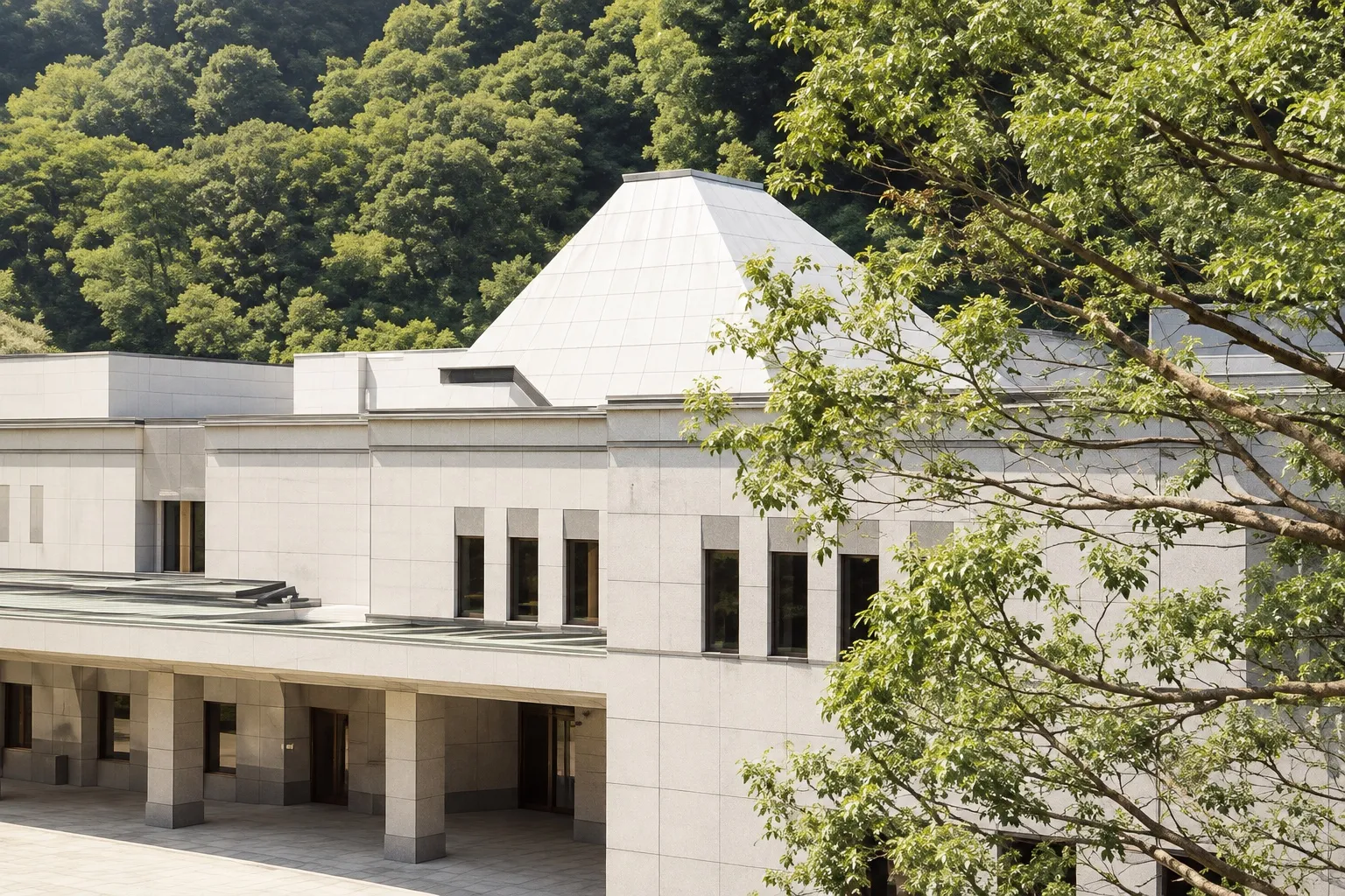 横浜市南部斎場の外観。緑の山を背にしたピラミッド形の屋根の建物（イメージ）